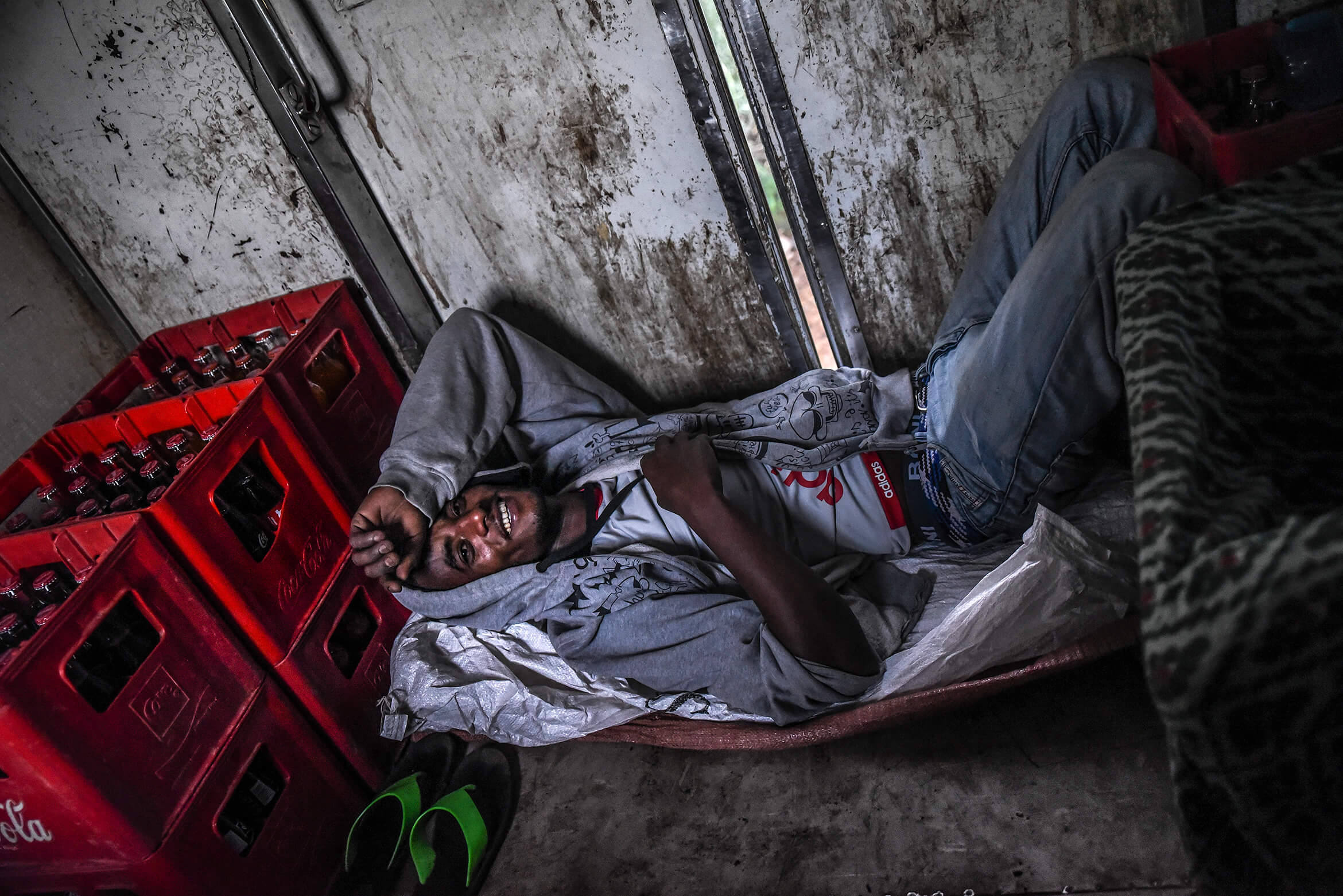 A passenger of the Negus train is resting on the train floor, next to numerous bottles of Coca-Cola that will be sold and drunk during the journey