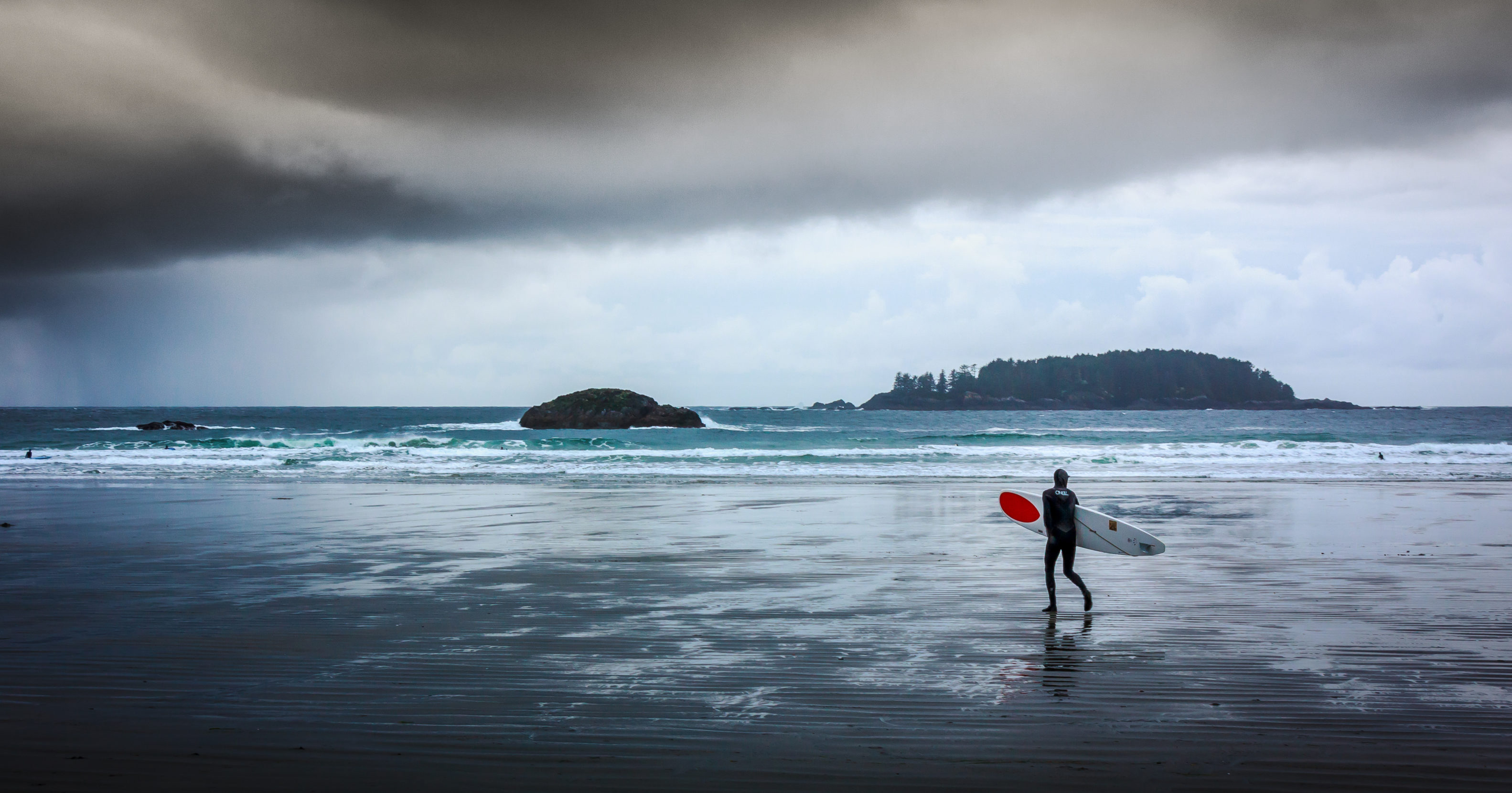A lone surfer approaches a coming storm on a Tofino beach. Dramatic skies and storm swells converge on the west coast of Vancouver Island each winter. Photo: Craig Whiteside.