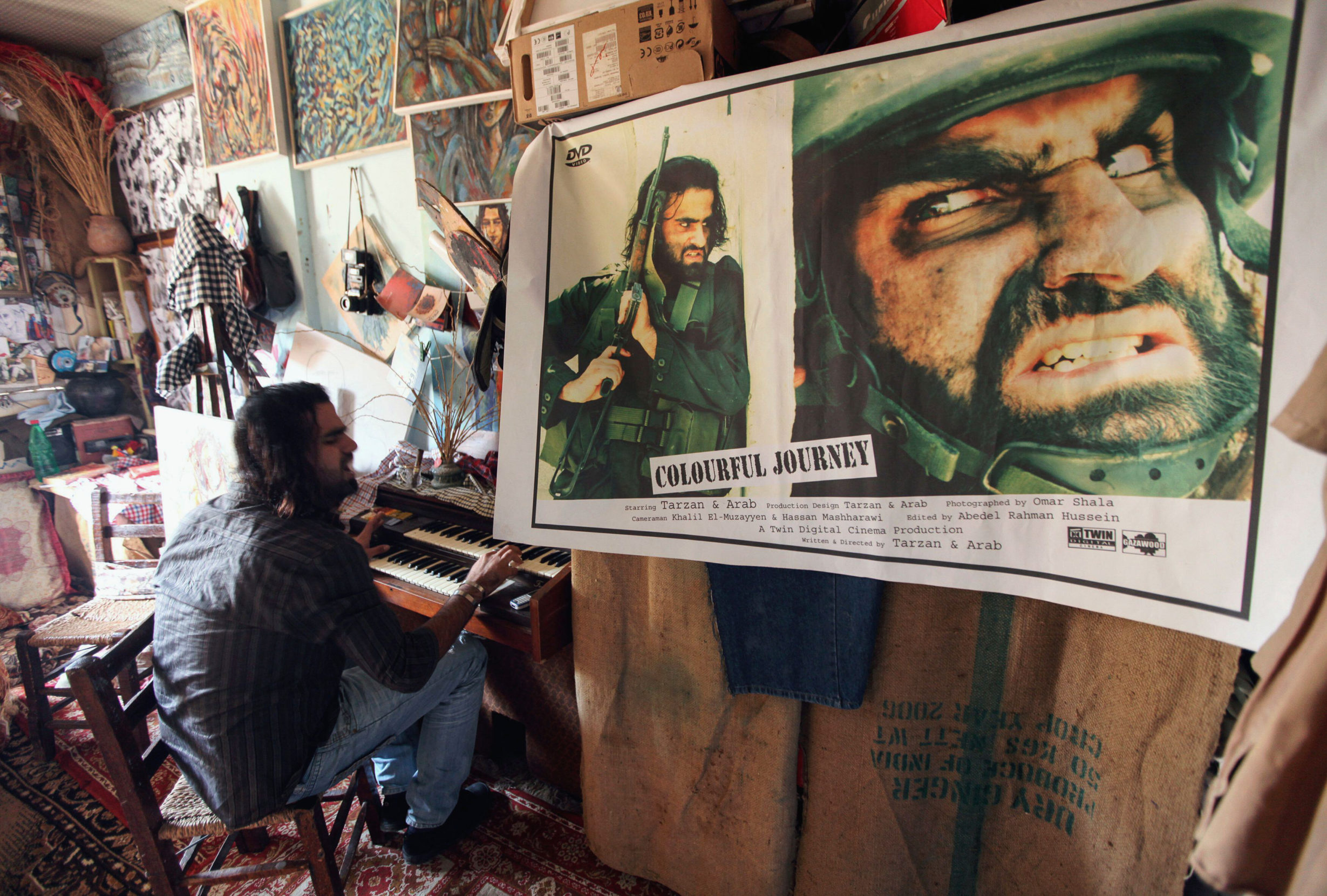 Tarzan plays piano in his Gaza home turned makeshift film studio, Gazawood, in 2010, where he and his brother conceived of a project that would create film posters for imagined films named after Israeli military operations. Photo: Mohammed Salem/Reuters/Alamy.