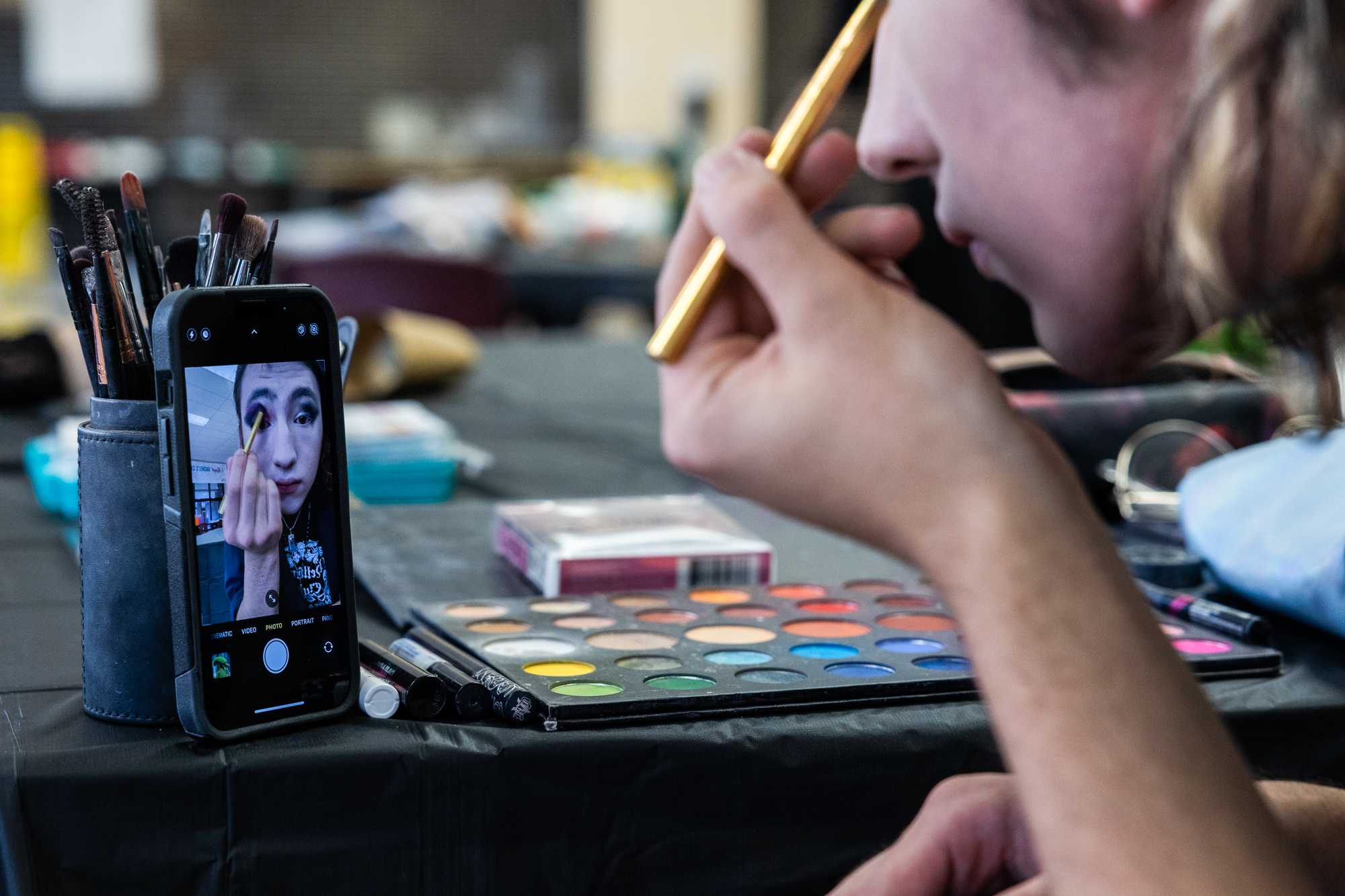 A young woman applies face paint using her phone's camera as a mirror.