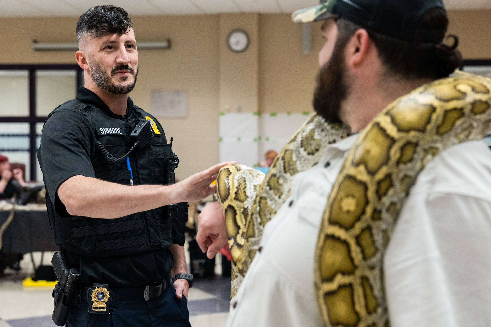 A detective in uniform admires a large snake on the shoulders of a man in the foreground.