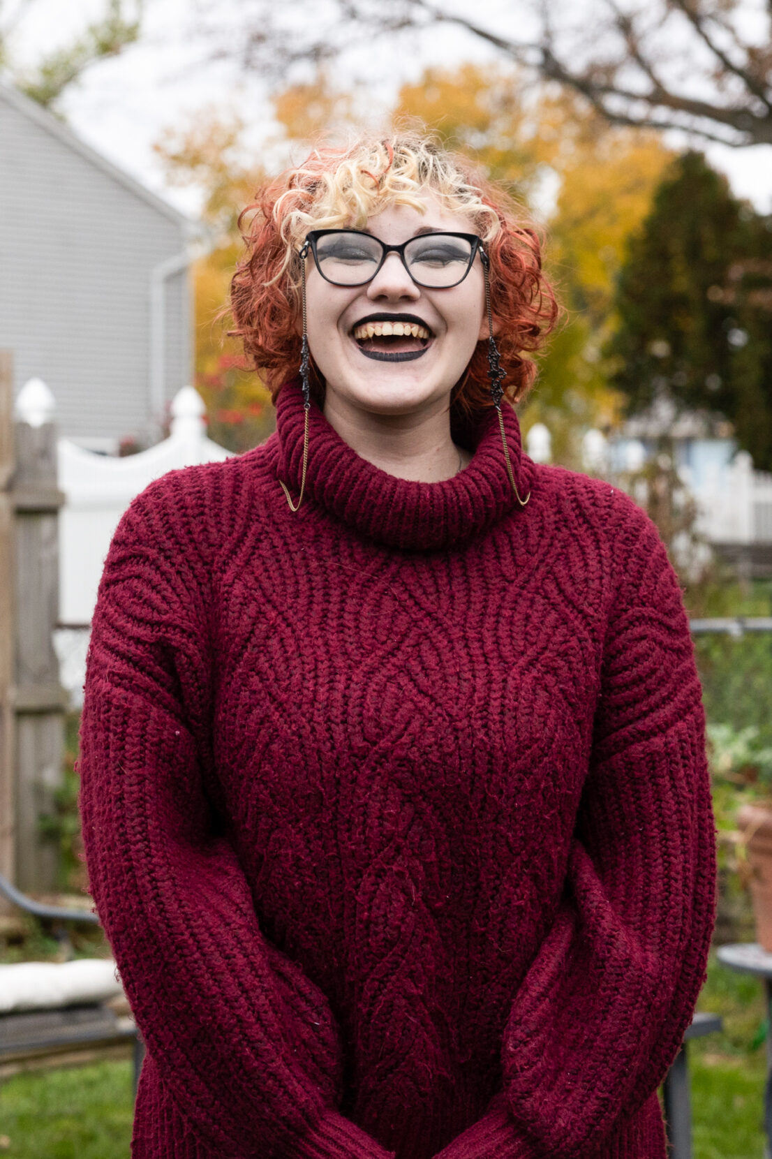 A portrait of a laughing woman with curly orange hair and glasses.