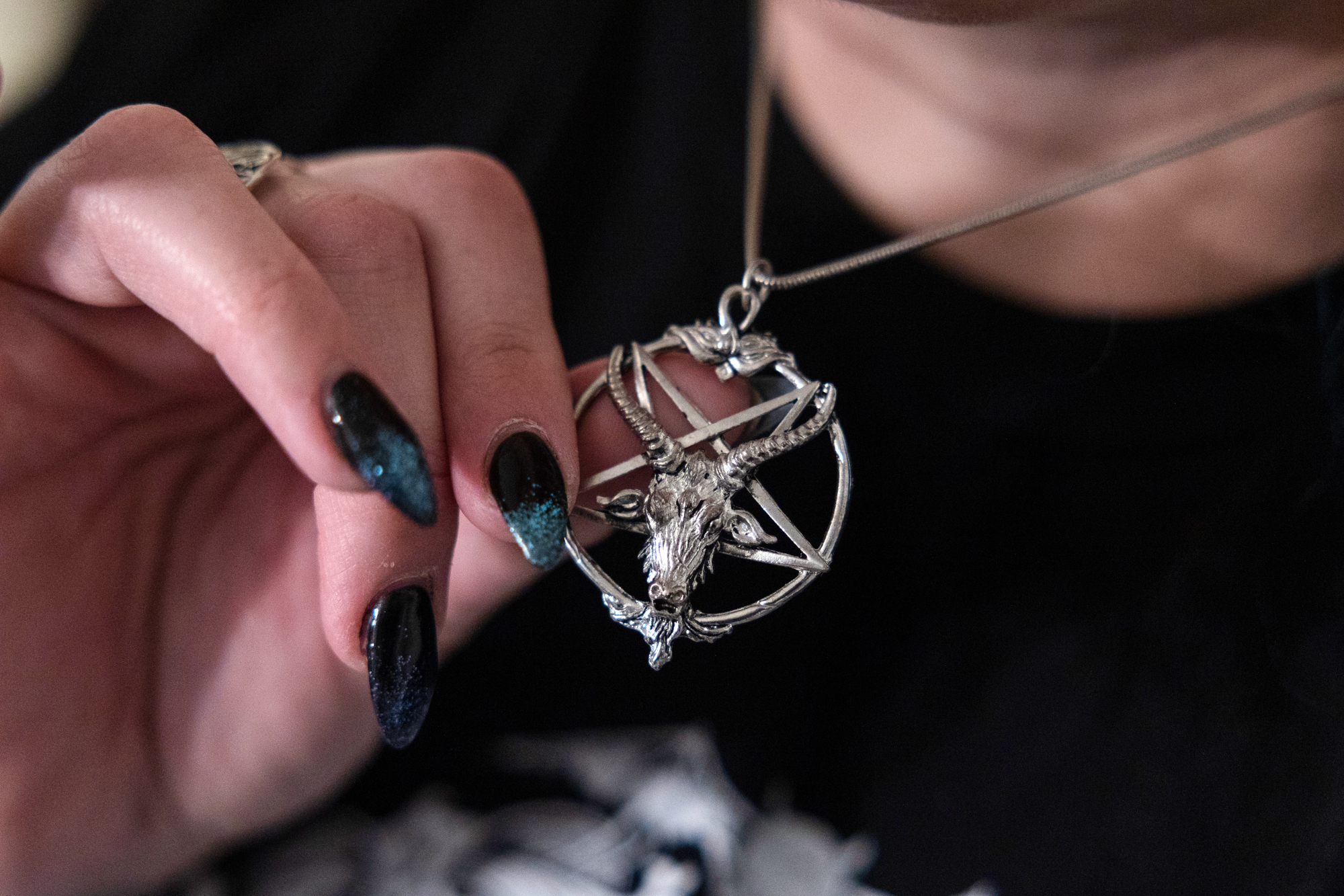 A woman's hand holding a silver baphomet necklace.