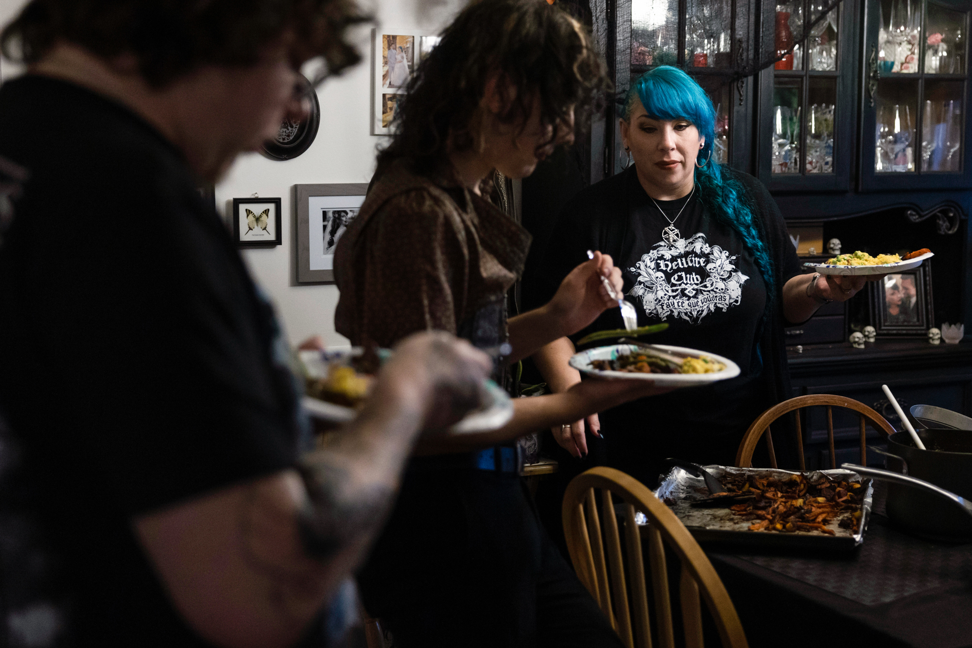 Two people serving themselves food on paper plates, and a woman with blue hair in the background.