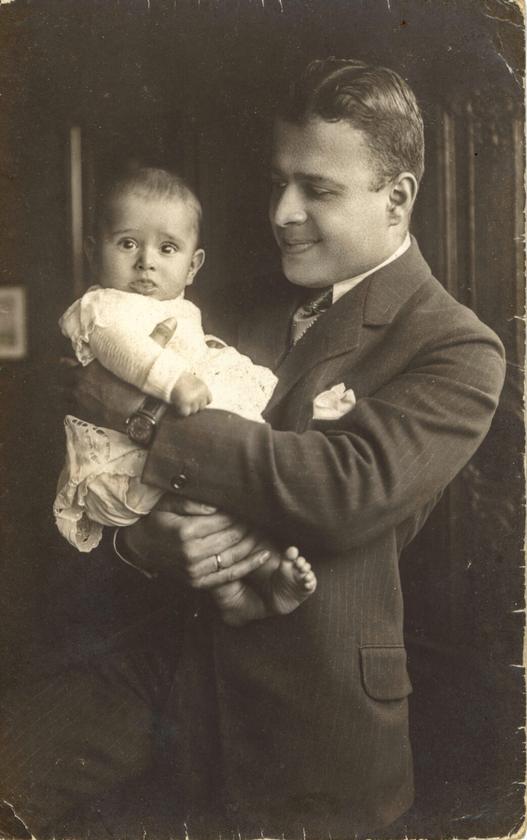 A black and white portrait of a man in a suit holding and admiring a baby.