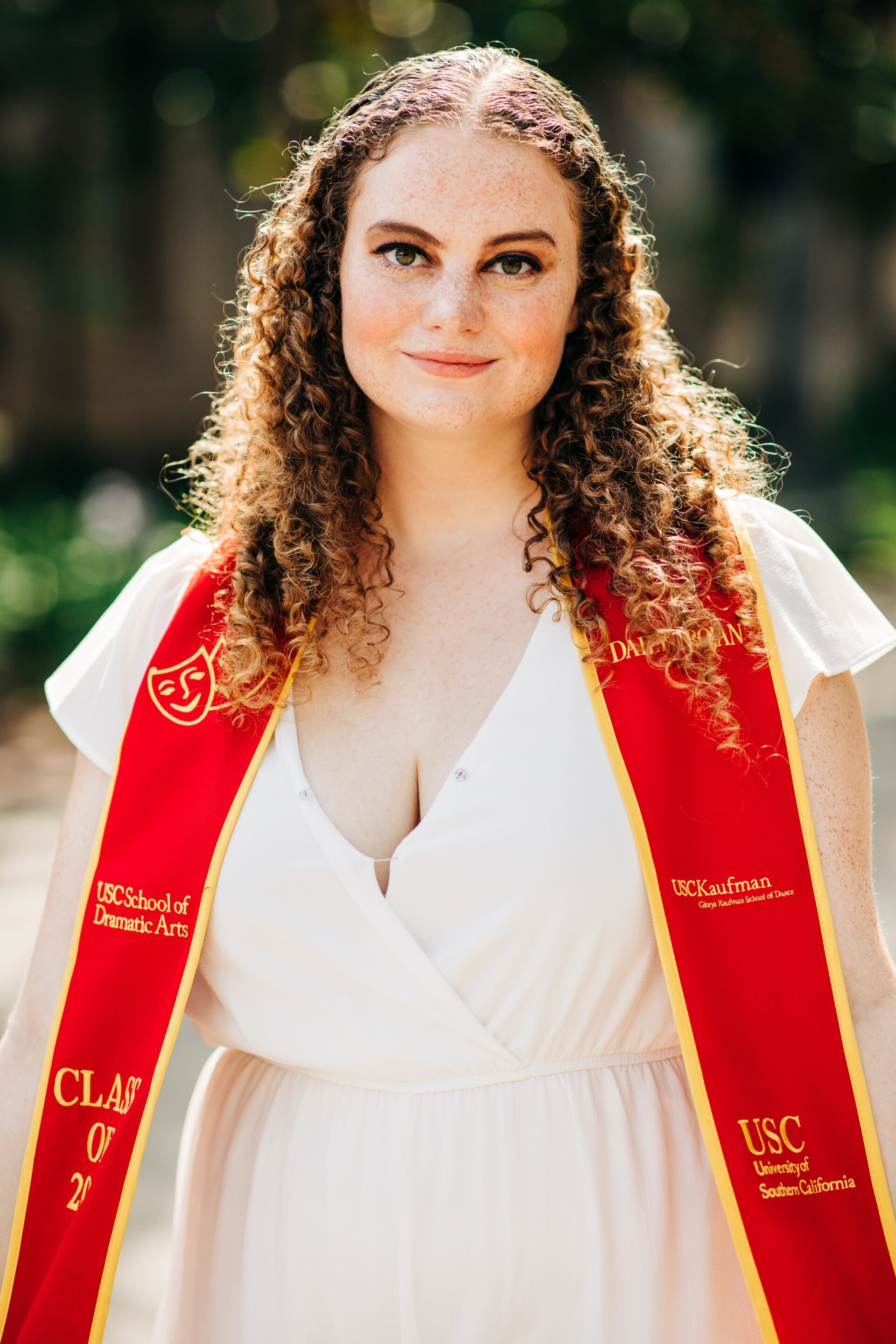 Portrait of a young woman with curly hair and a red graduation stole reading 