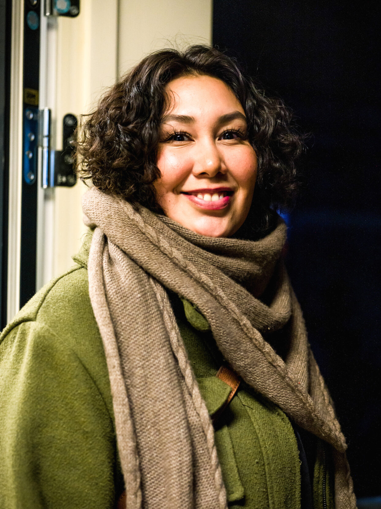 A portrait of a smiling young woman with a gray scarf and curly black hair.