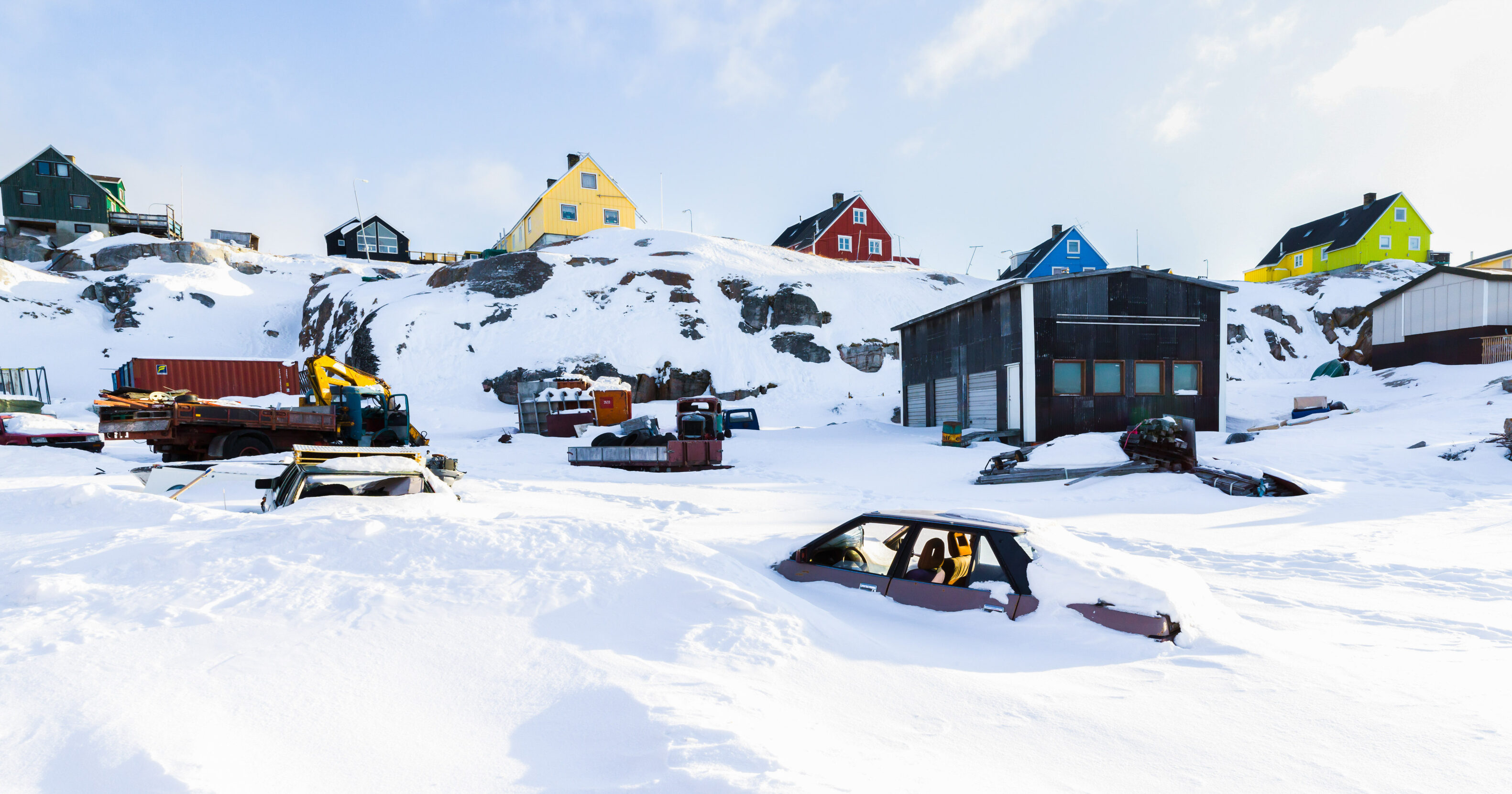 Fresh snow blankets a landscape of brightly colored buildings and snow-covered cars.