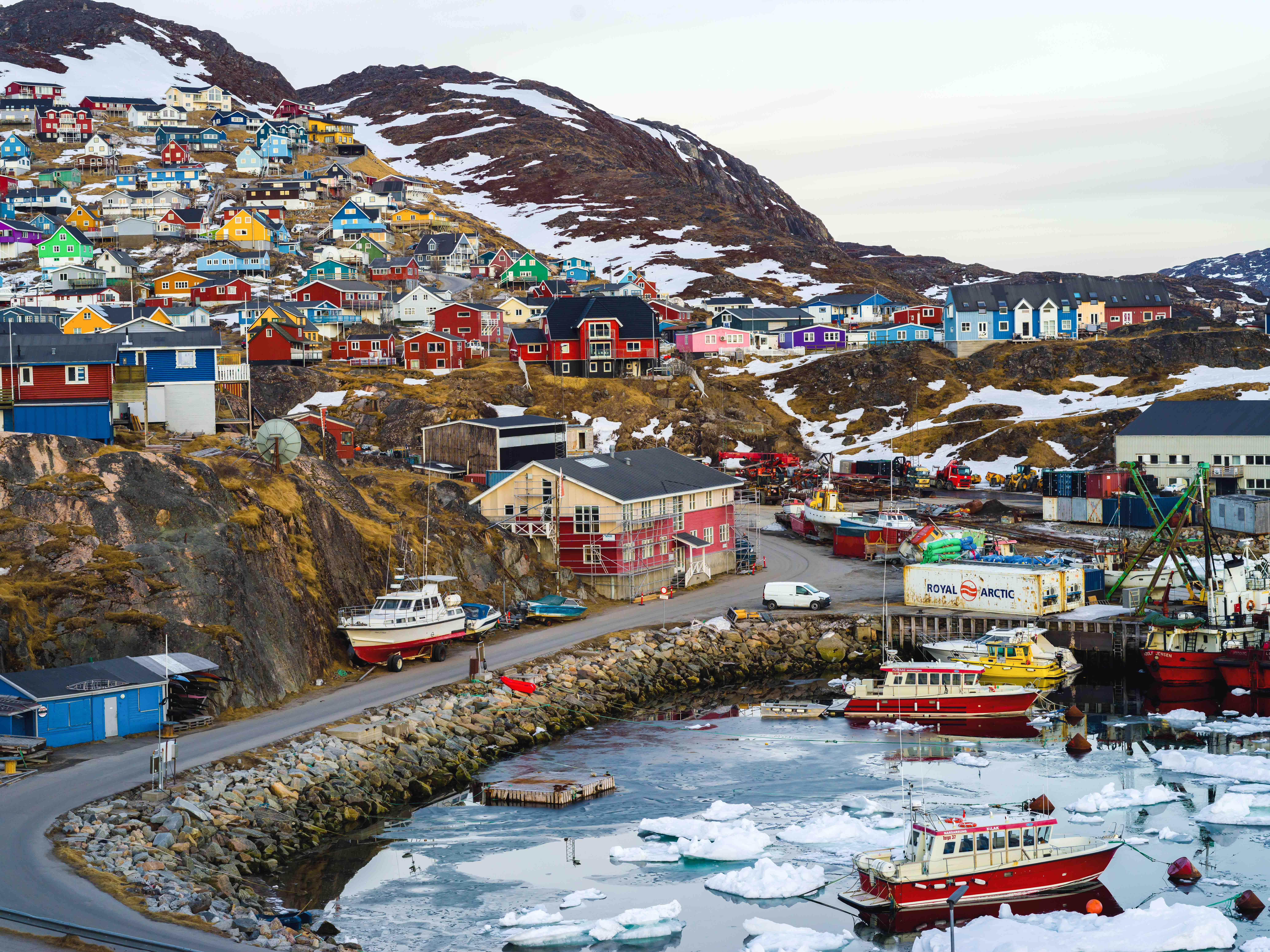a town of colorful homes sits against the icy waters of its bay.