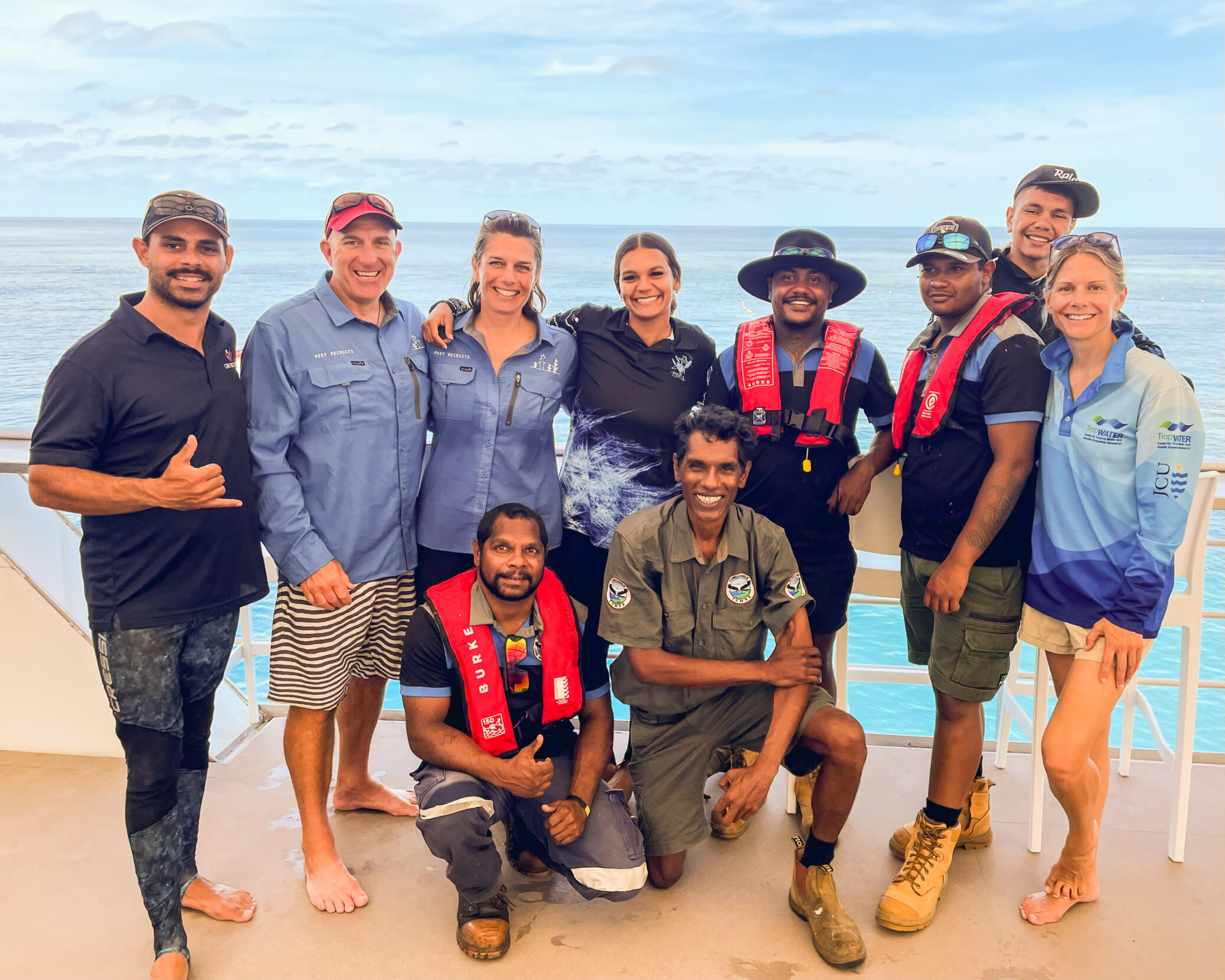A team of scientists and sea rangers poses for a group photo on a boat deck.