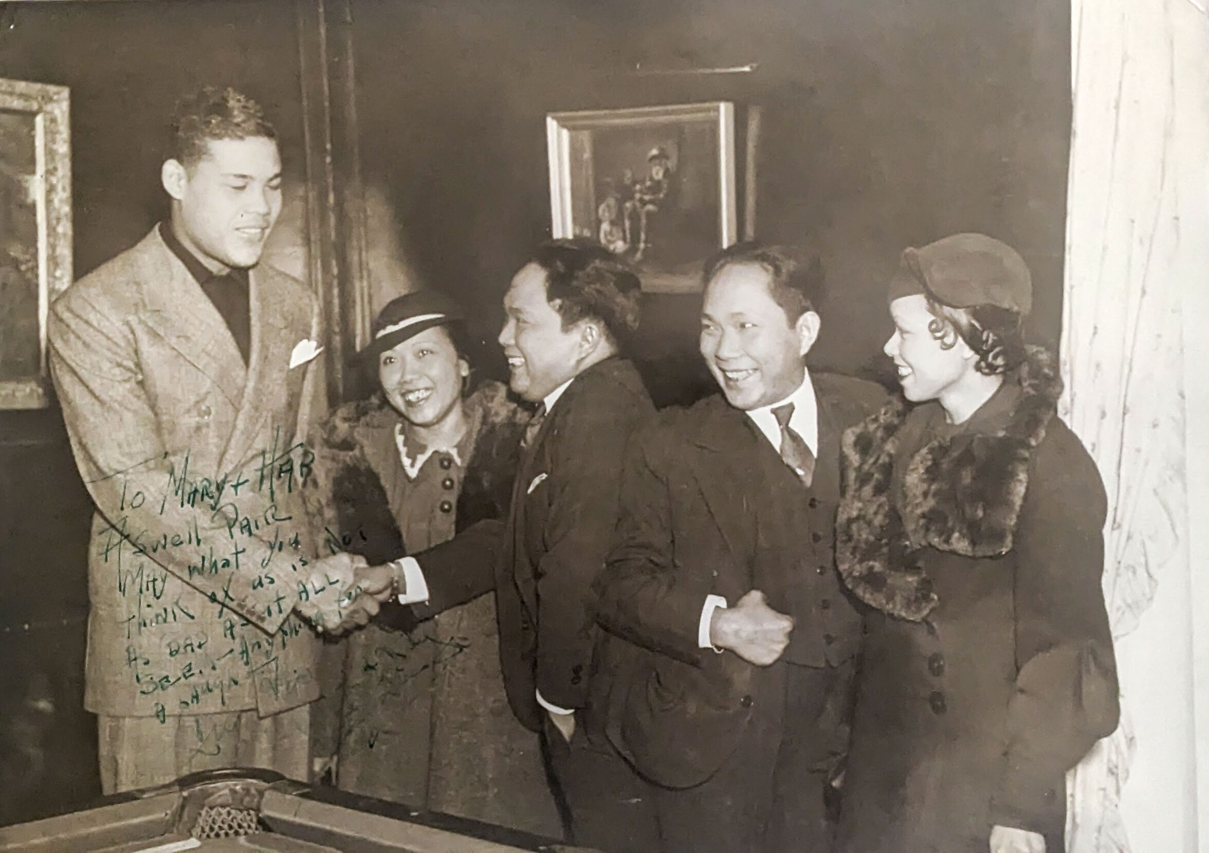 A signed black and white photograph of conjoined twins with their wives beside them, shaking hands with a tall Black man.