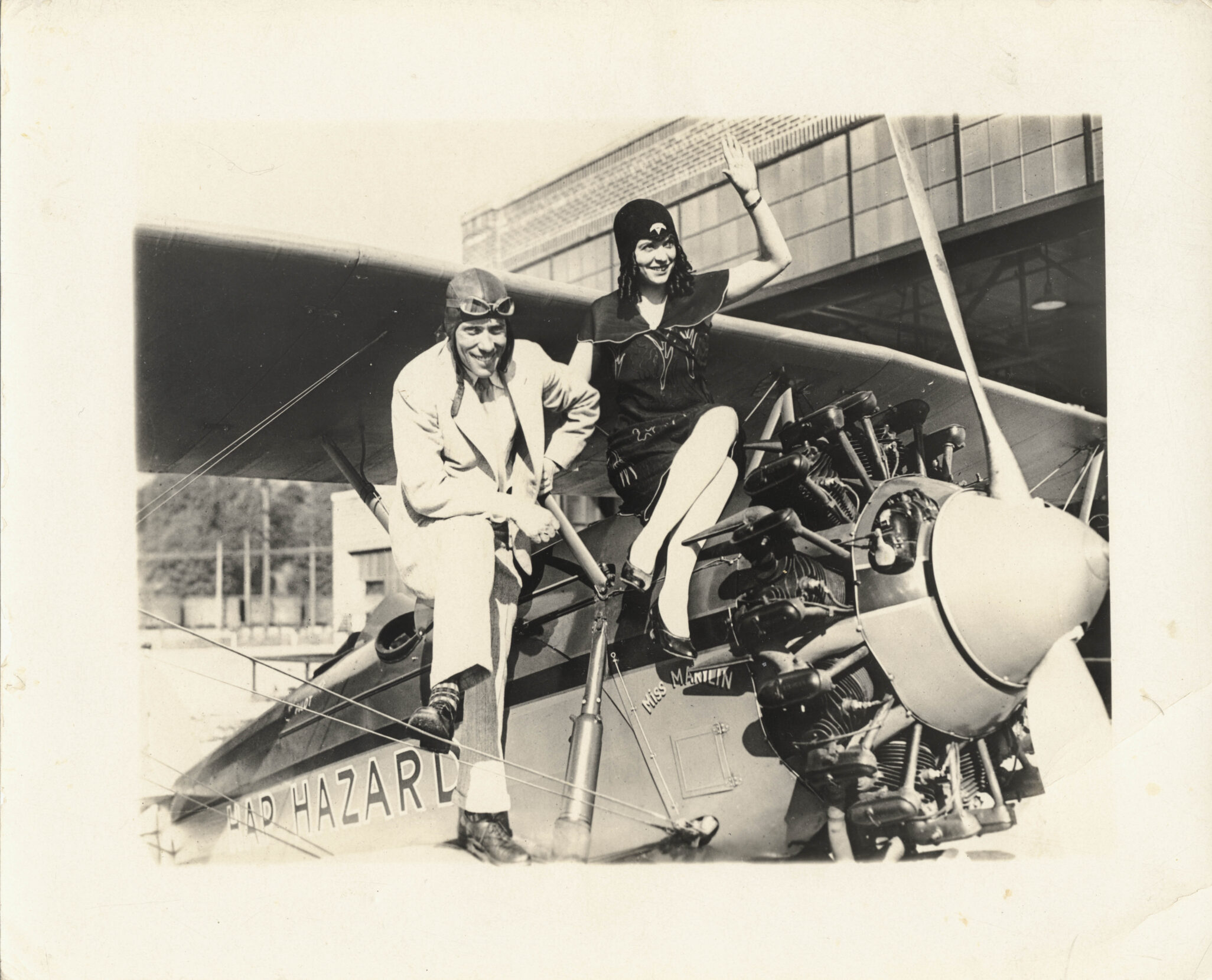 Black and white photo of a couple sitting atop a propeller plane.