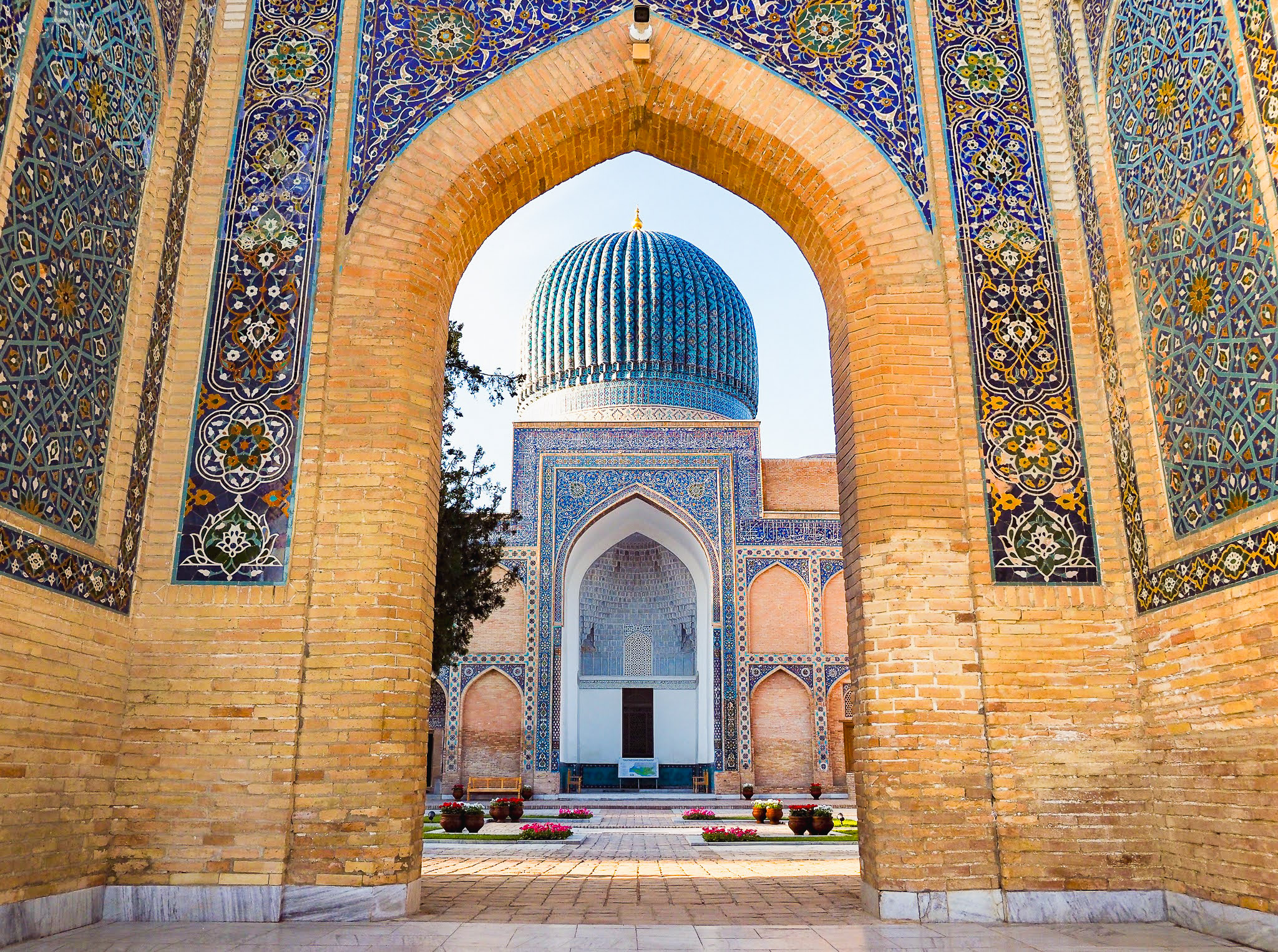 A blue domed mausoleum framed by a brick archway and intricate, geometrical design.