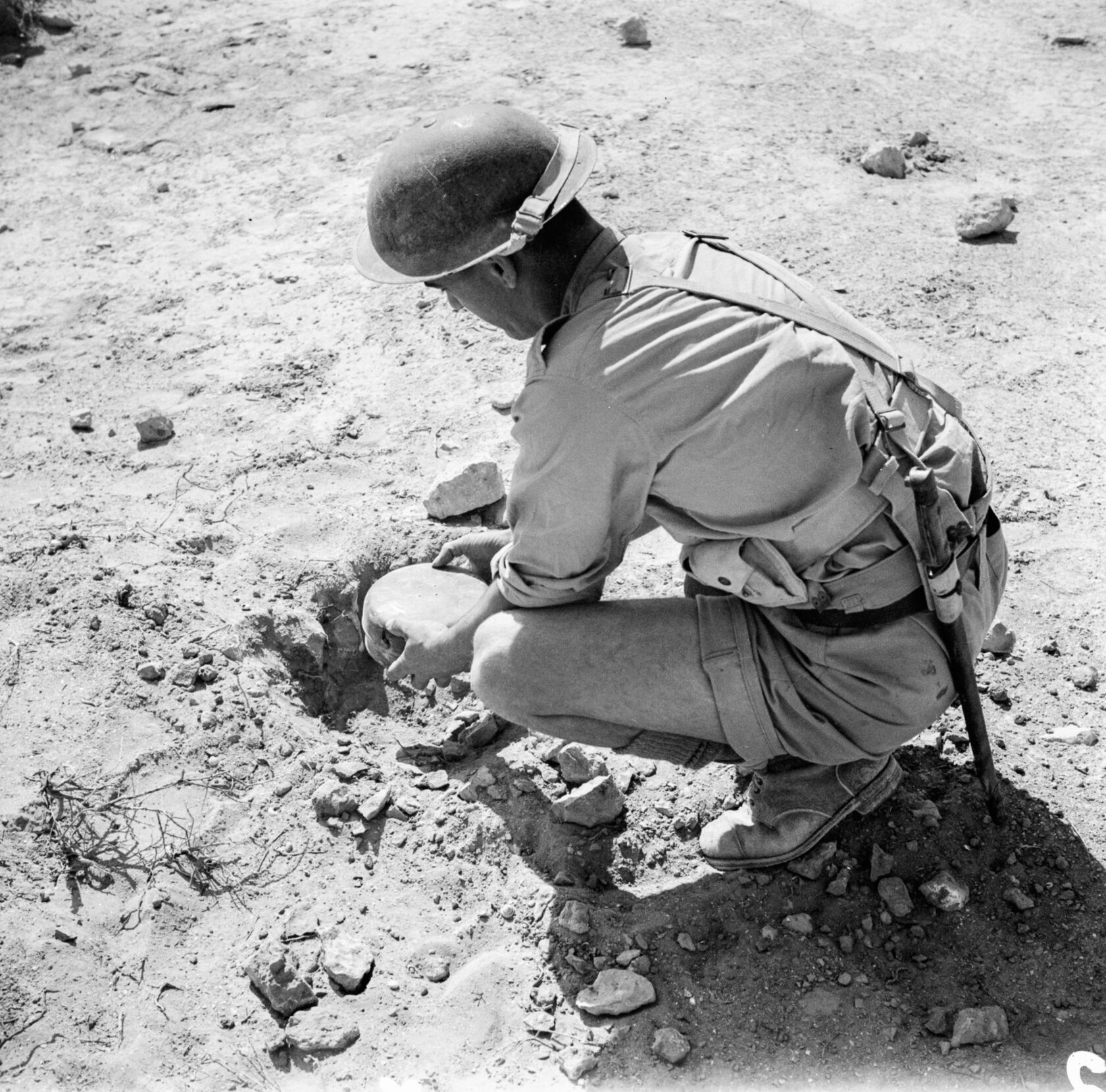 Black and white photo of a soldier placing an anti-tank mine into a hole in the ground.
