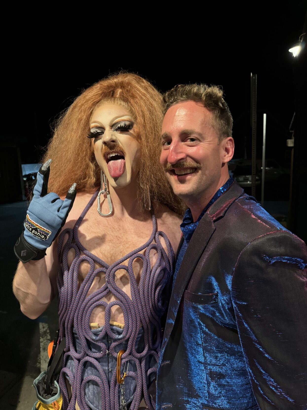 Drag queen and man in velvet jacket posing for photo.