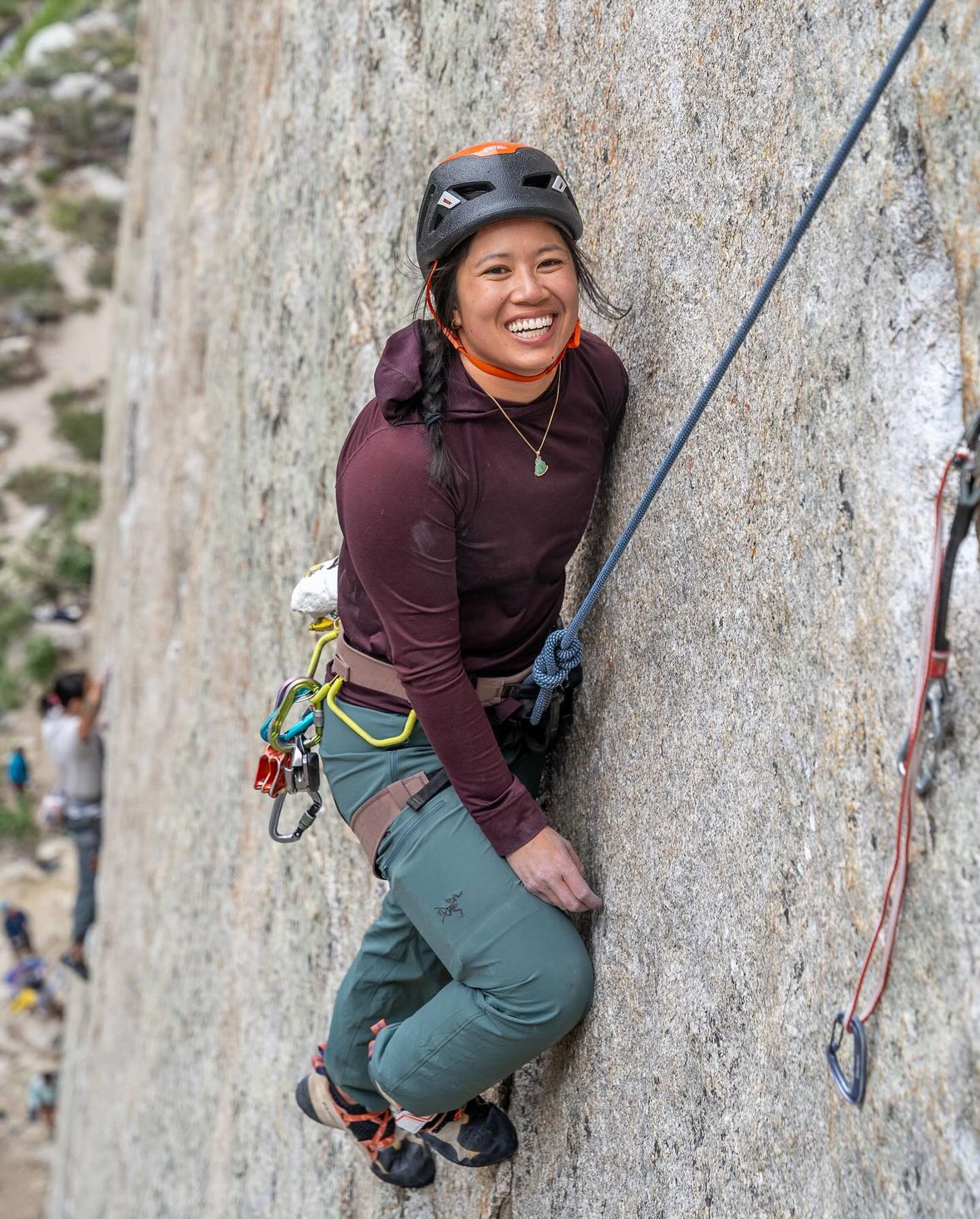 A woman smiling while rock climbing.