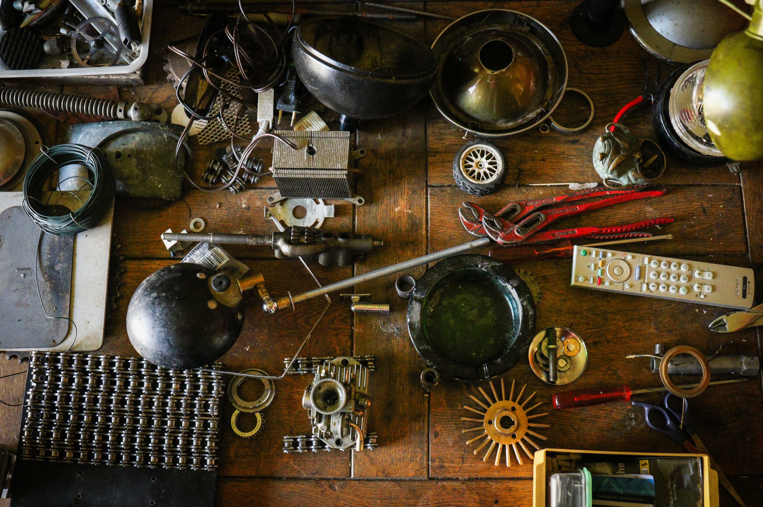 A tabletop cluttered with odds and ends including wires, a wrench, a remote control, and various metal parts.