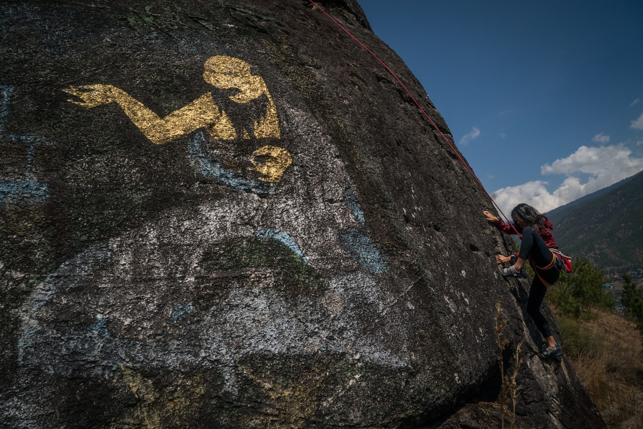 A woman climbs a rock with a figure painted on it.