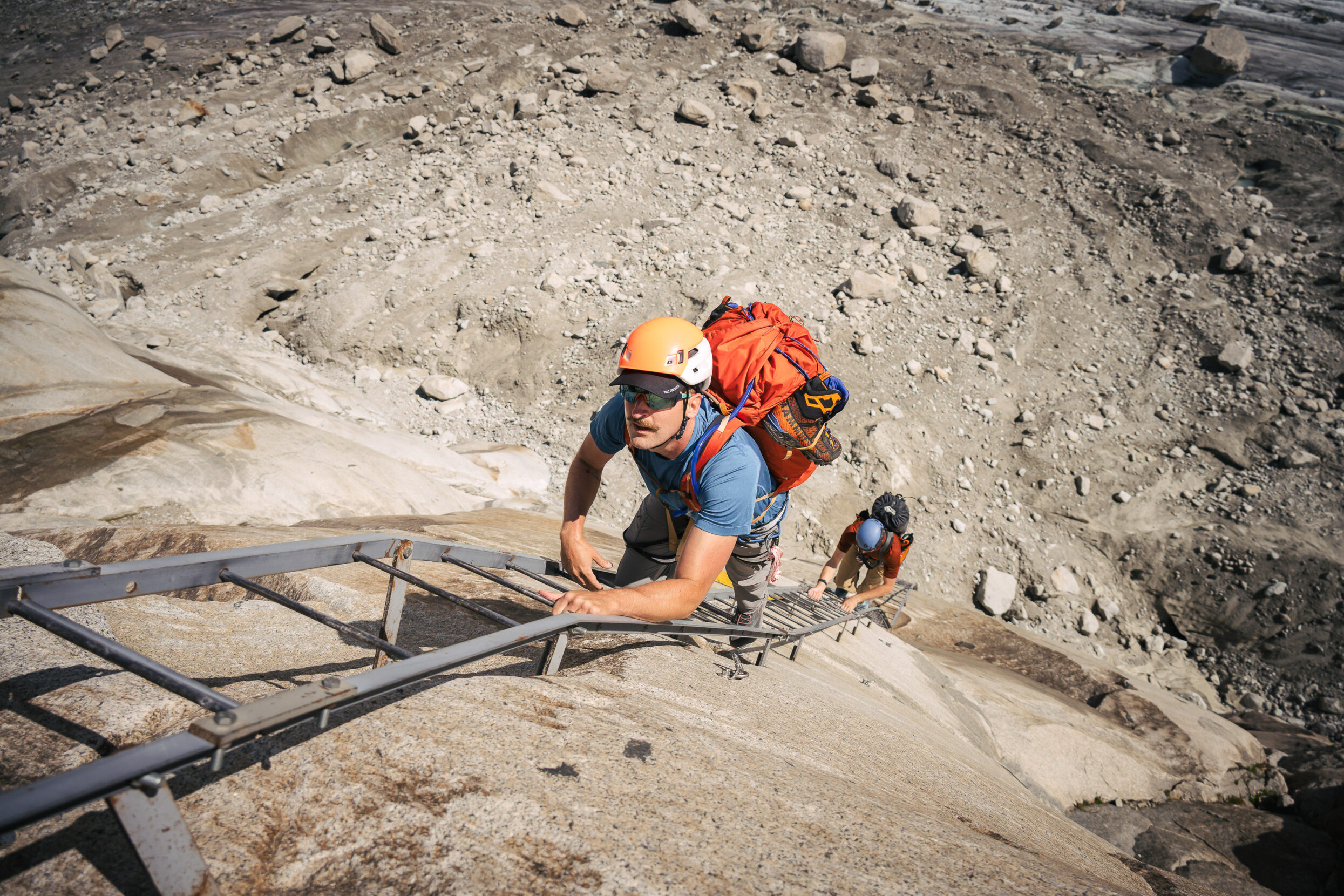 Two men climb a ladder up a mountain side.