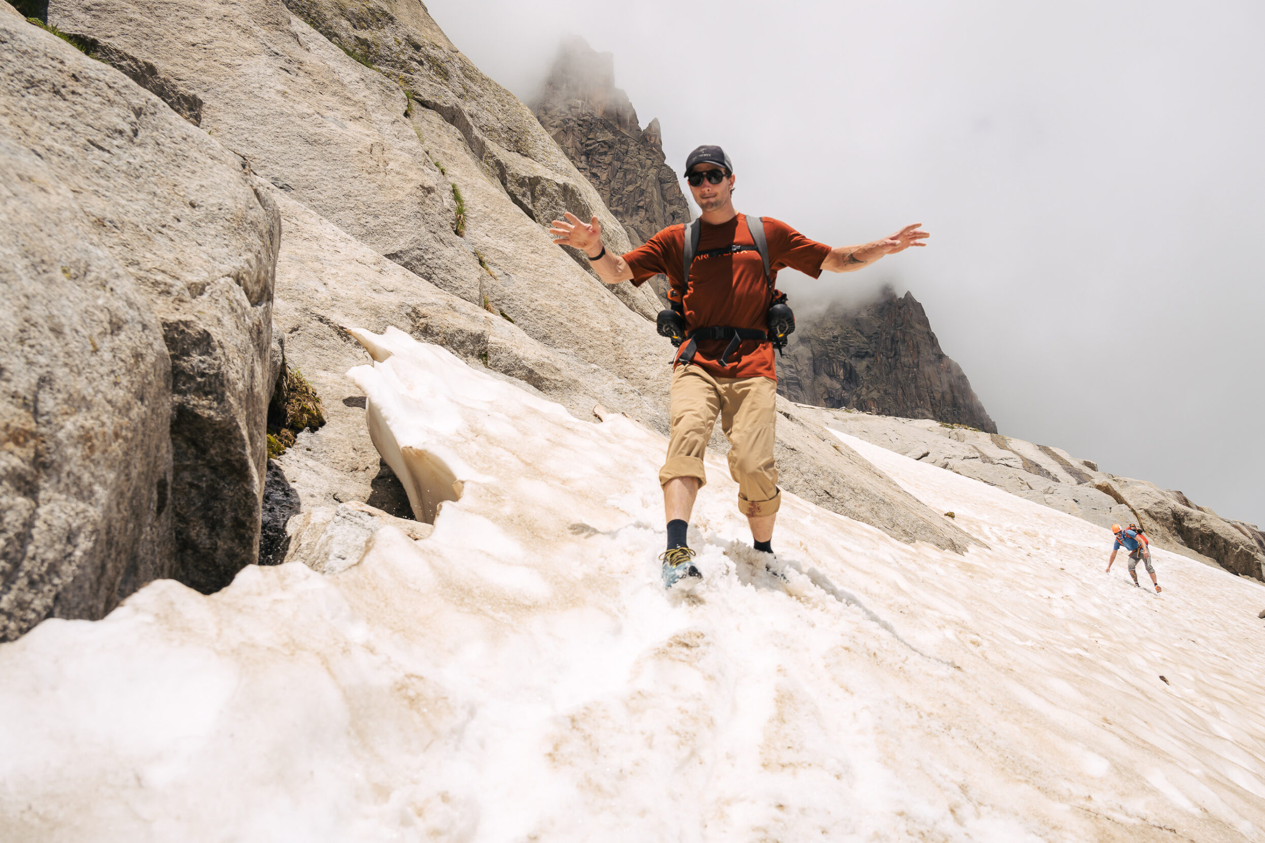 A man in maroon glissades across the glacier.