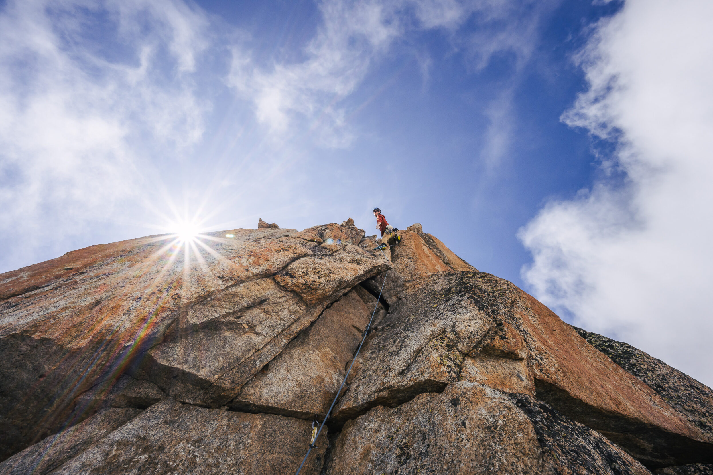 a climber up on a mountain summit with the sun peaking over the mountain.