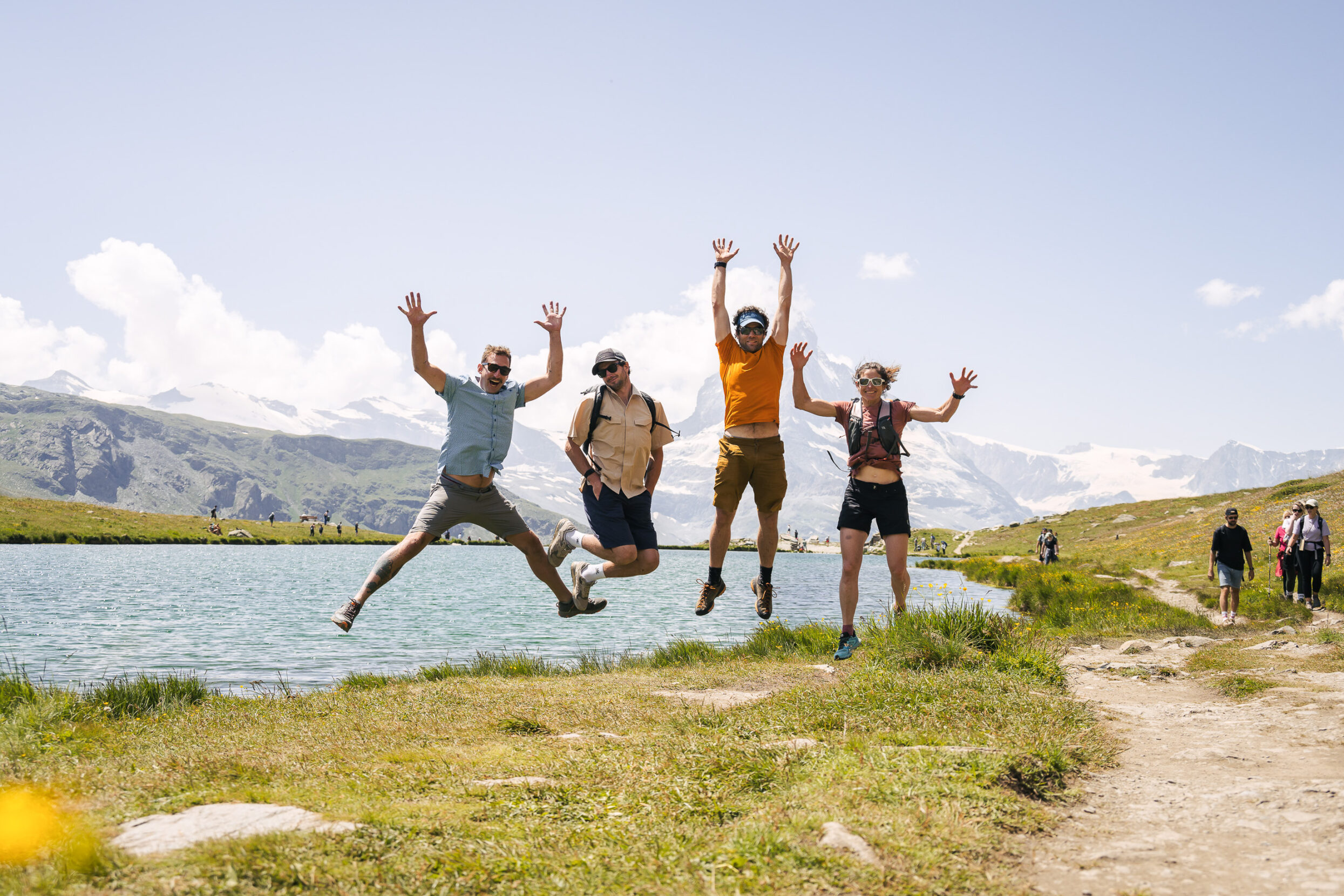 Three men and a woman leaping in the air in front of a lake.