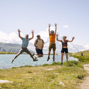 Three men and a woman leaping in the air in front of a lake.