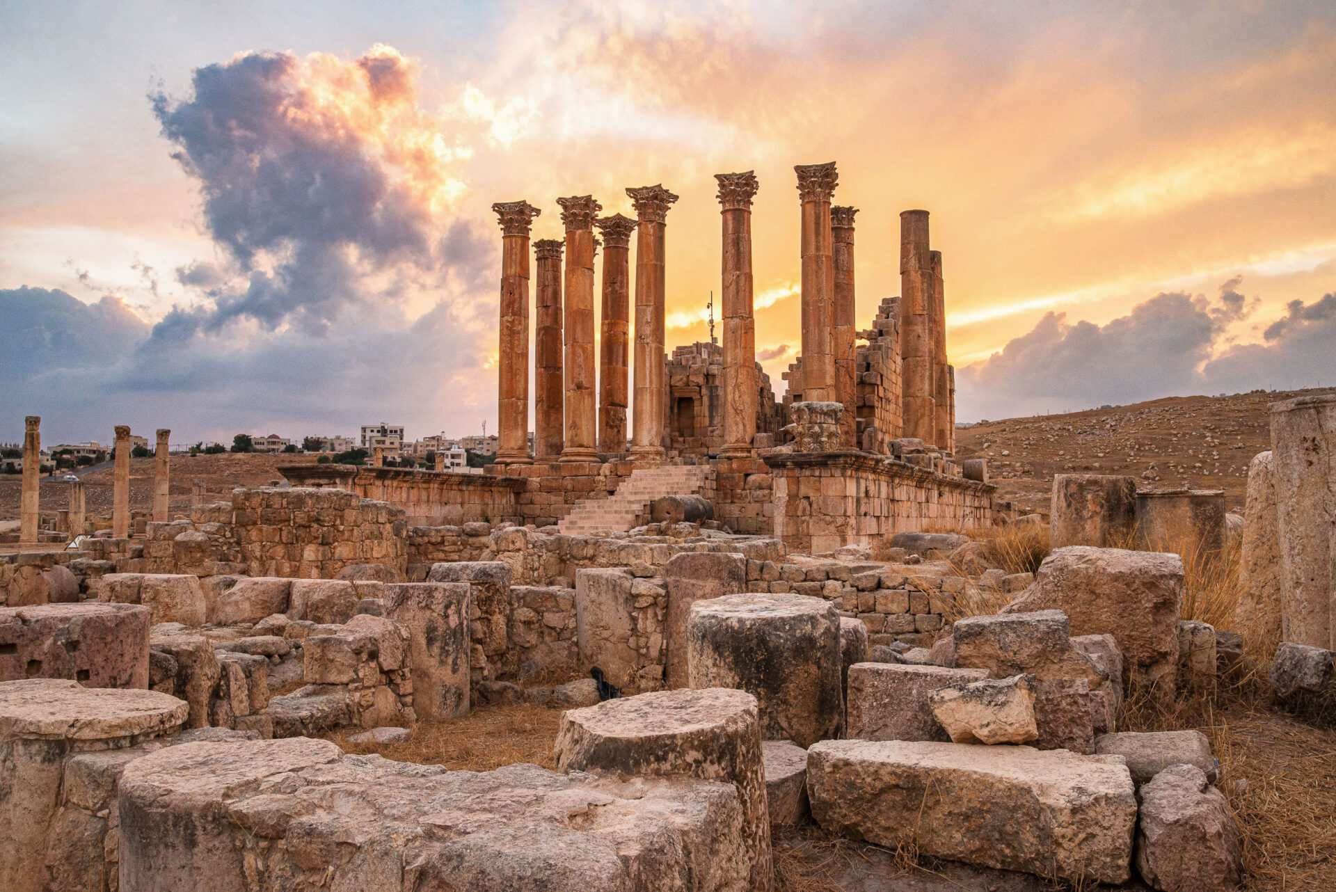 Ancient ruins and columns rise before golden sunlight.