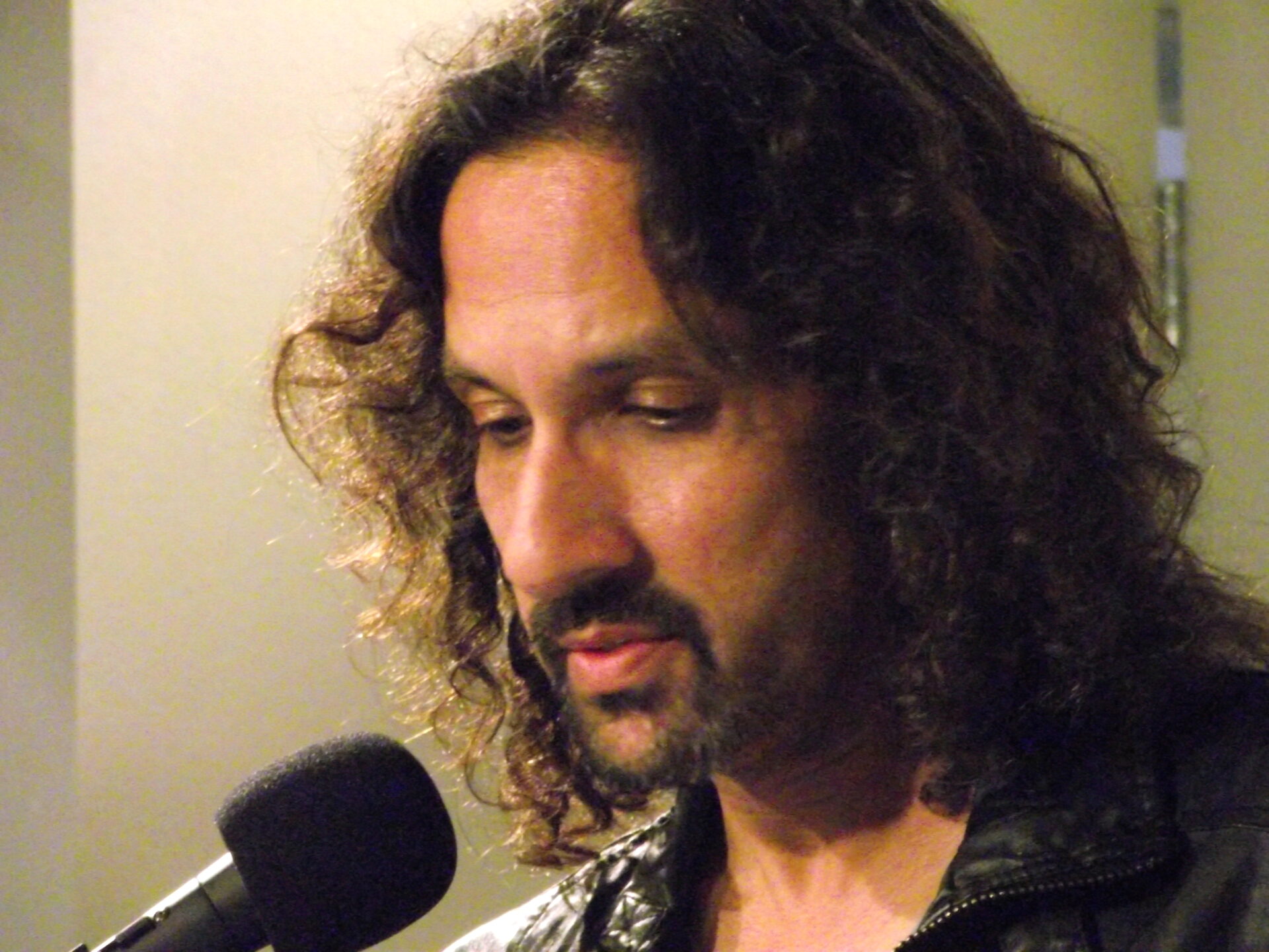 Close up of man with dark curly hair, mustache and beard, before a microphone.