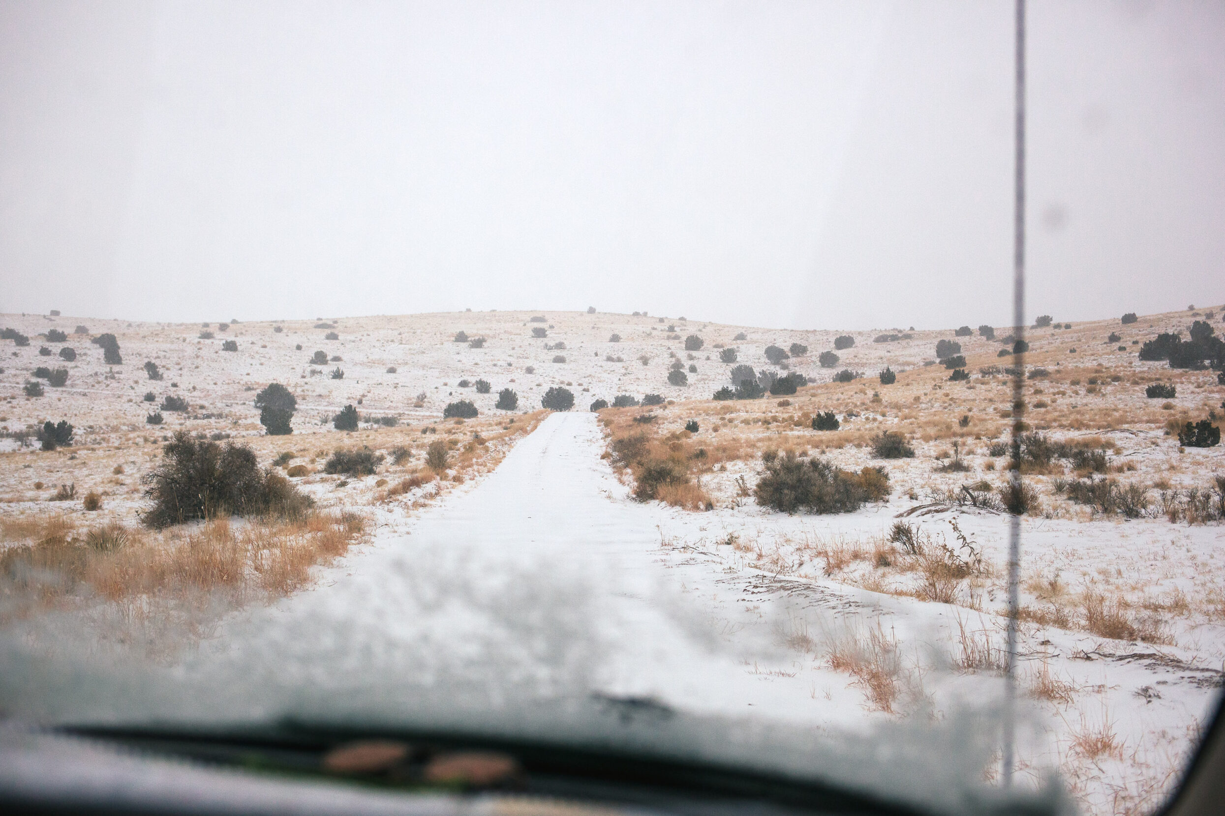 A desert road covered in snow from the viewpoint of a car's dash.