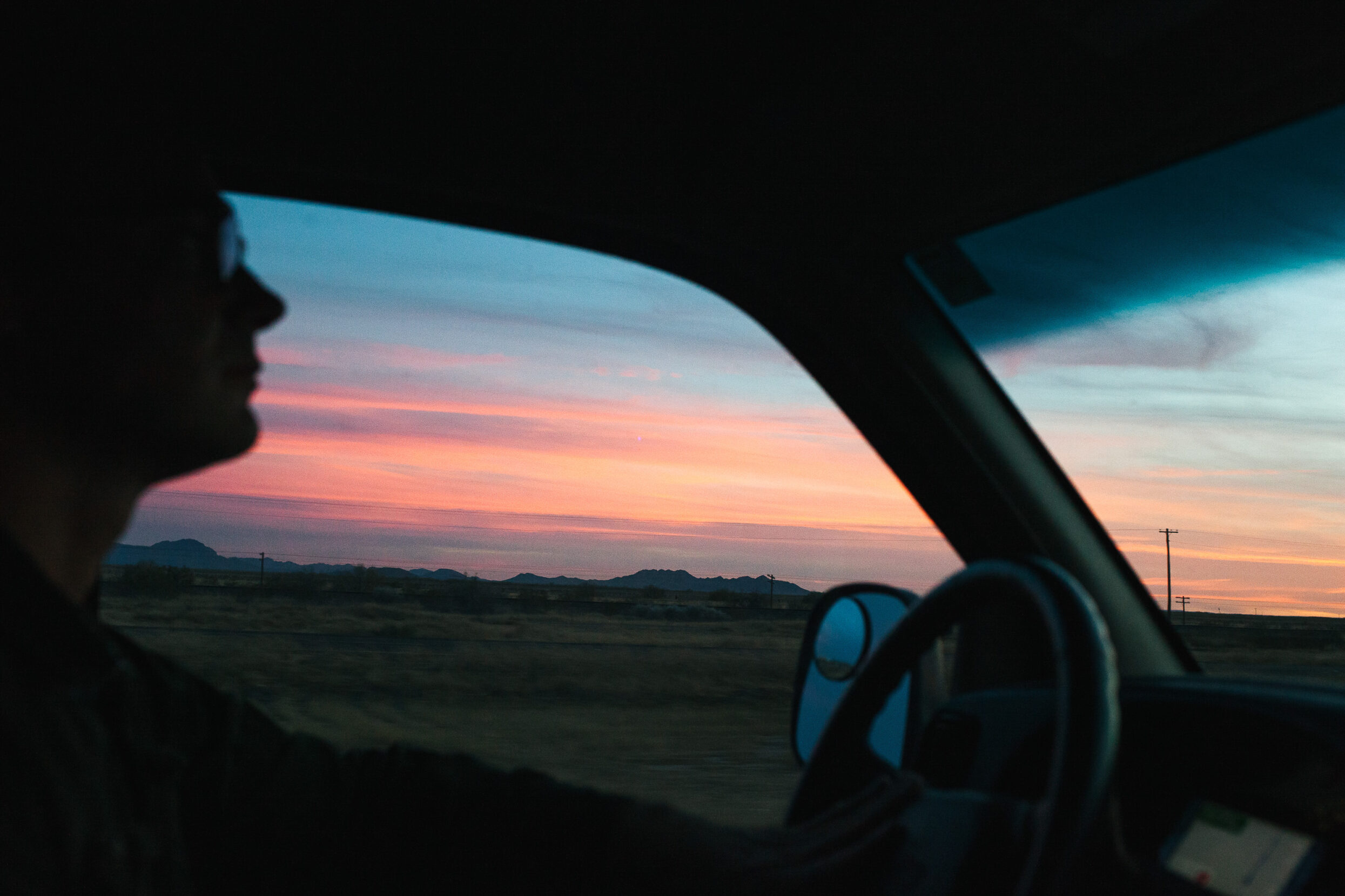 The silhouette of a driver behind the wheel at sunset.