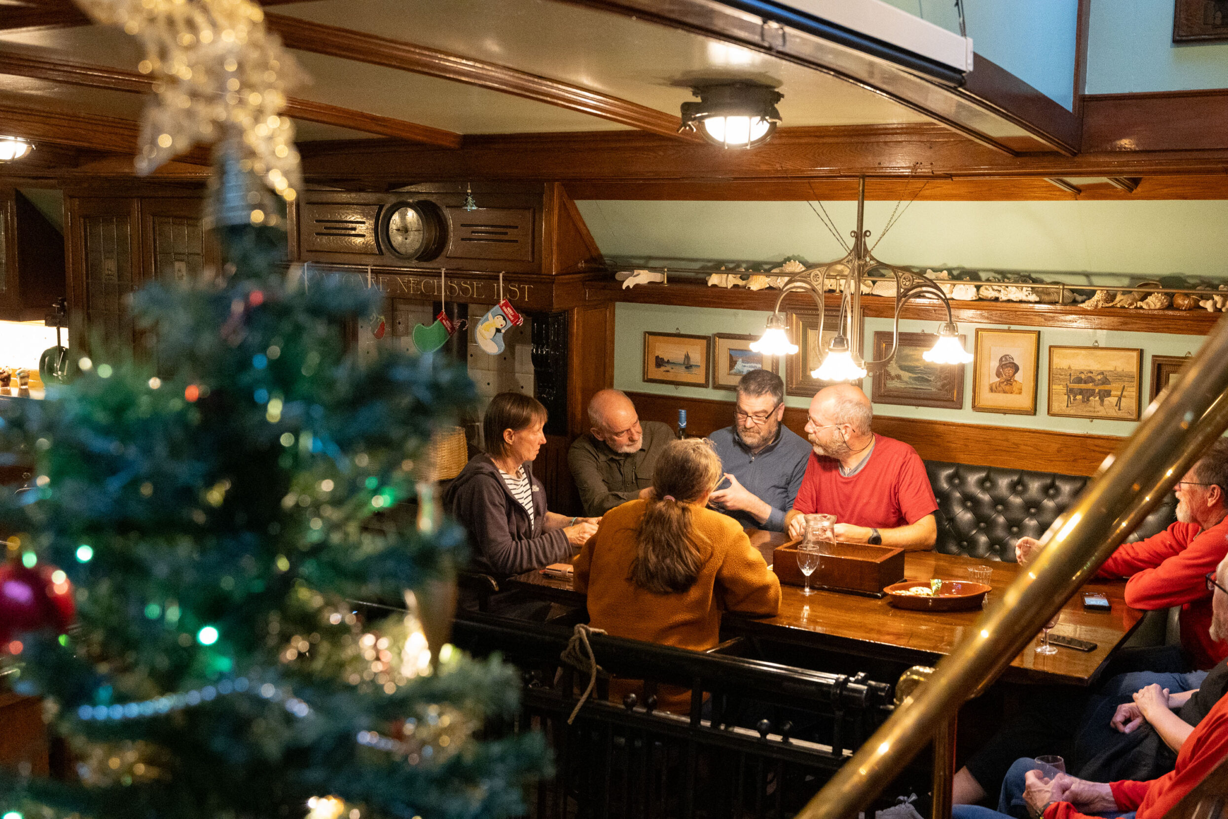 A group of seven people gathered around a dining table with a decorated Christmas tree in the foreground.