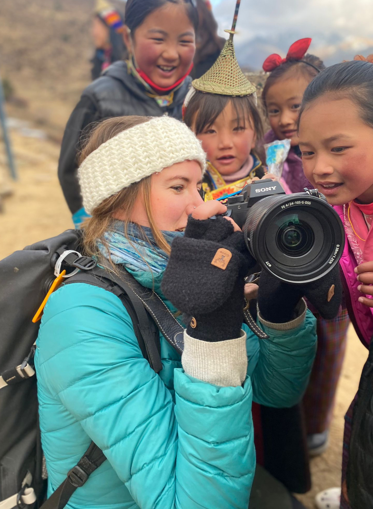 A woman holding a camera shows the screen to a group of children.