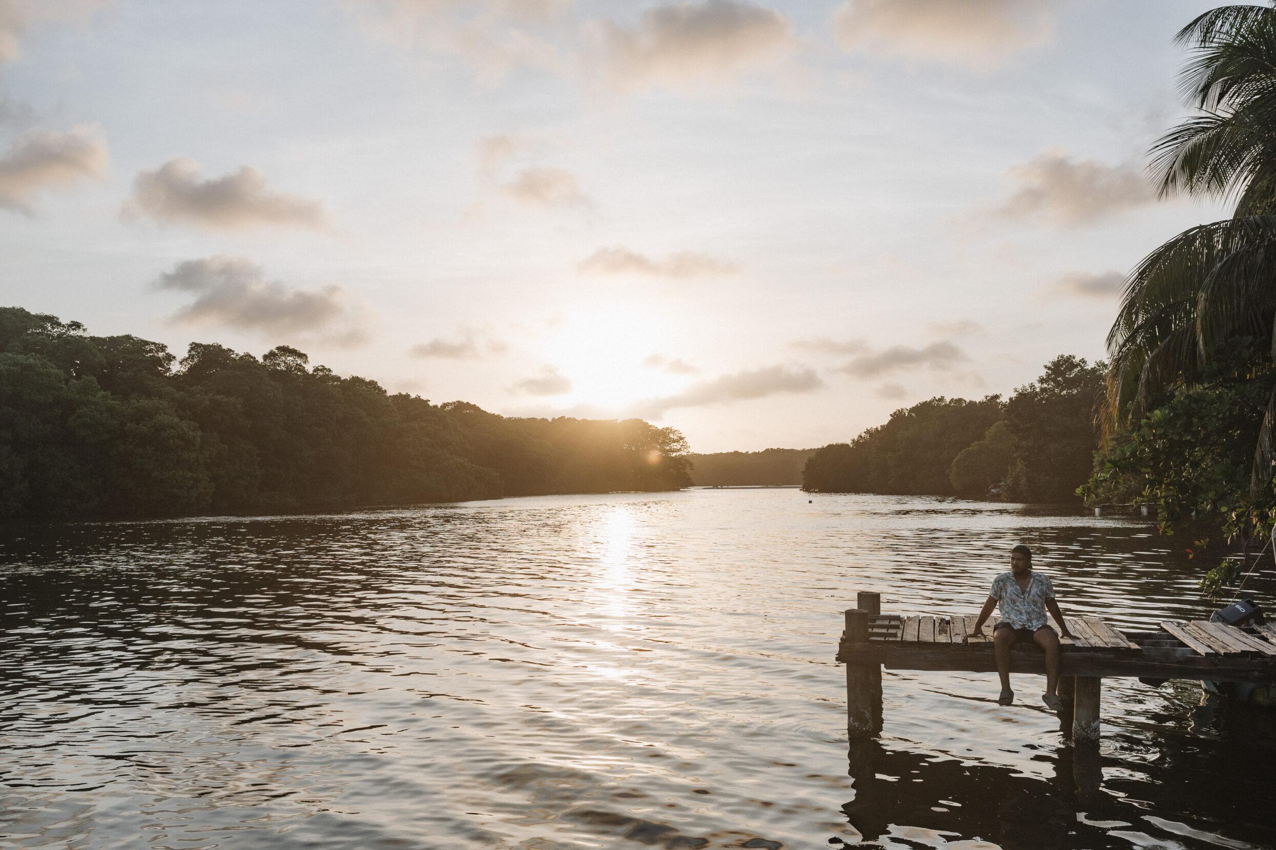 a man sitting on a dock as the sun sets behind him