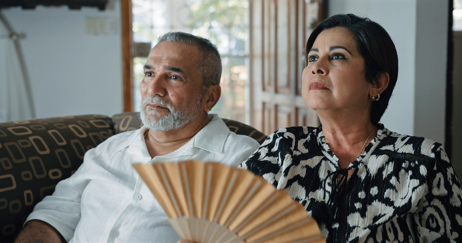 A man and a woman sitting on a sofa with a fan