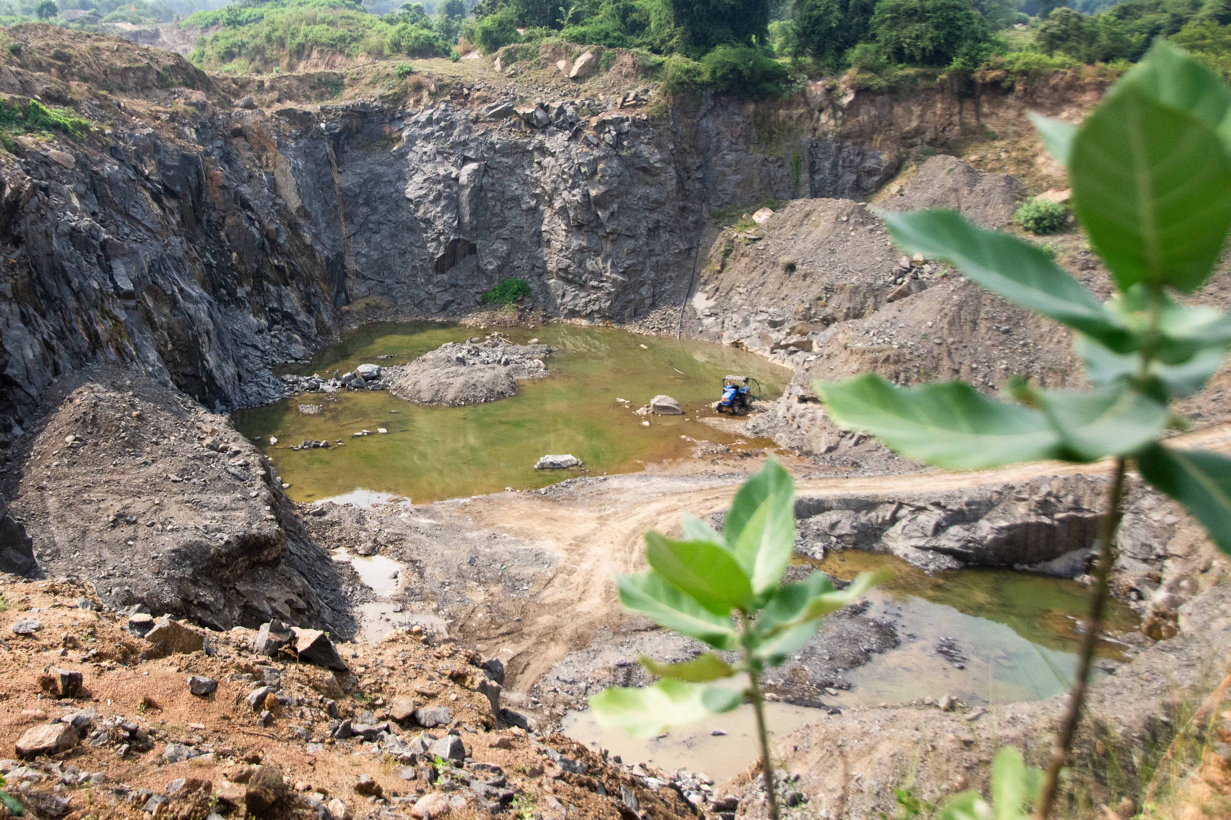 A large pit in the ground with green-brown water pooling at the bottom.